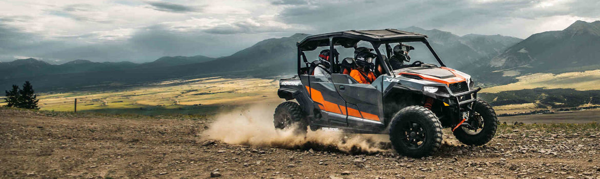 Four individuals offroading in a Polaris® UTV through clouded hills.